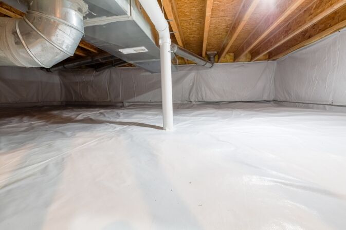 Crawl space with exposed wooden beams, ducts, and pipes, covered floor and walls with white plastic vapor barrier for moisture protection.