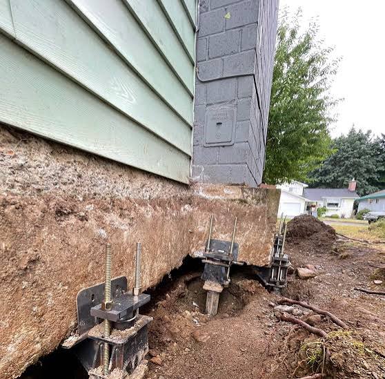 Close-up view of a house foundation with exposed soil and steel piers installed for structural support and stabilization.