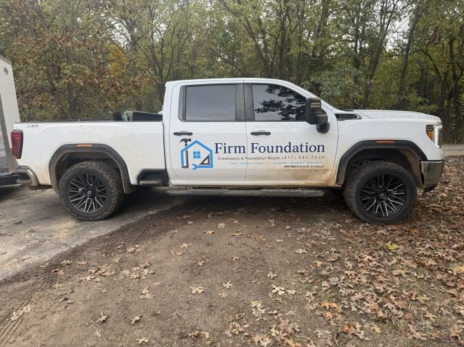 White pickup truck with Firm Foundation company logo and contact information parked on a leaf-covered ground near trees.