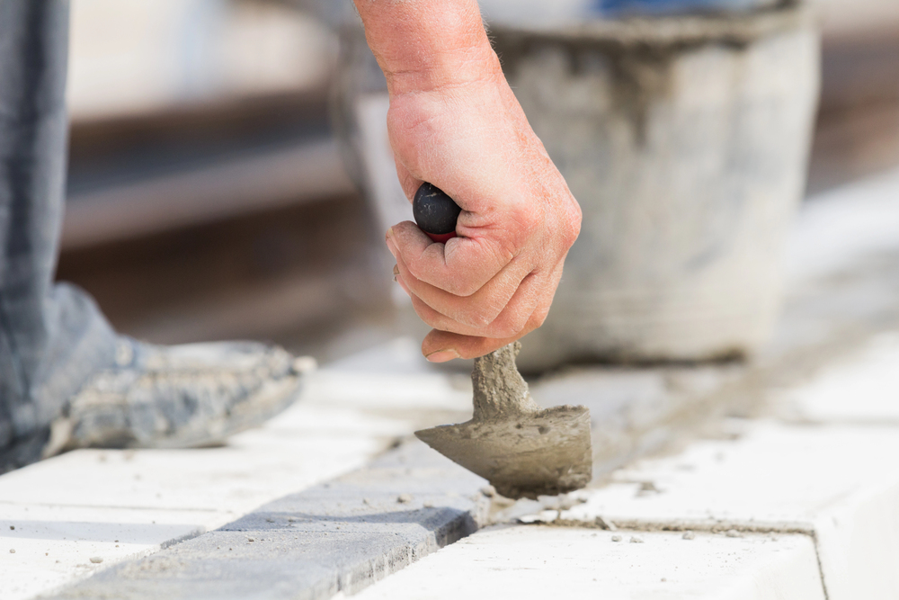 Close-up of a person using a trowel to apply mortar between concrete blocks at a construction site.