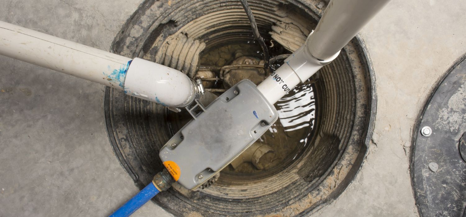 Overhead view of a sump pump system installed in a circular pit with PVC pipes and an electrical control box, partially surrounded by concrete floor—an essential component for basement waterproofing Joplin MO homeowners trust.